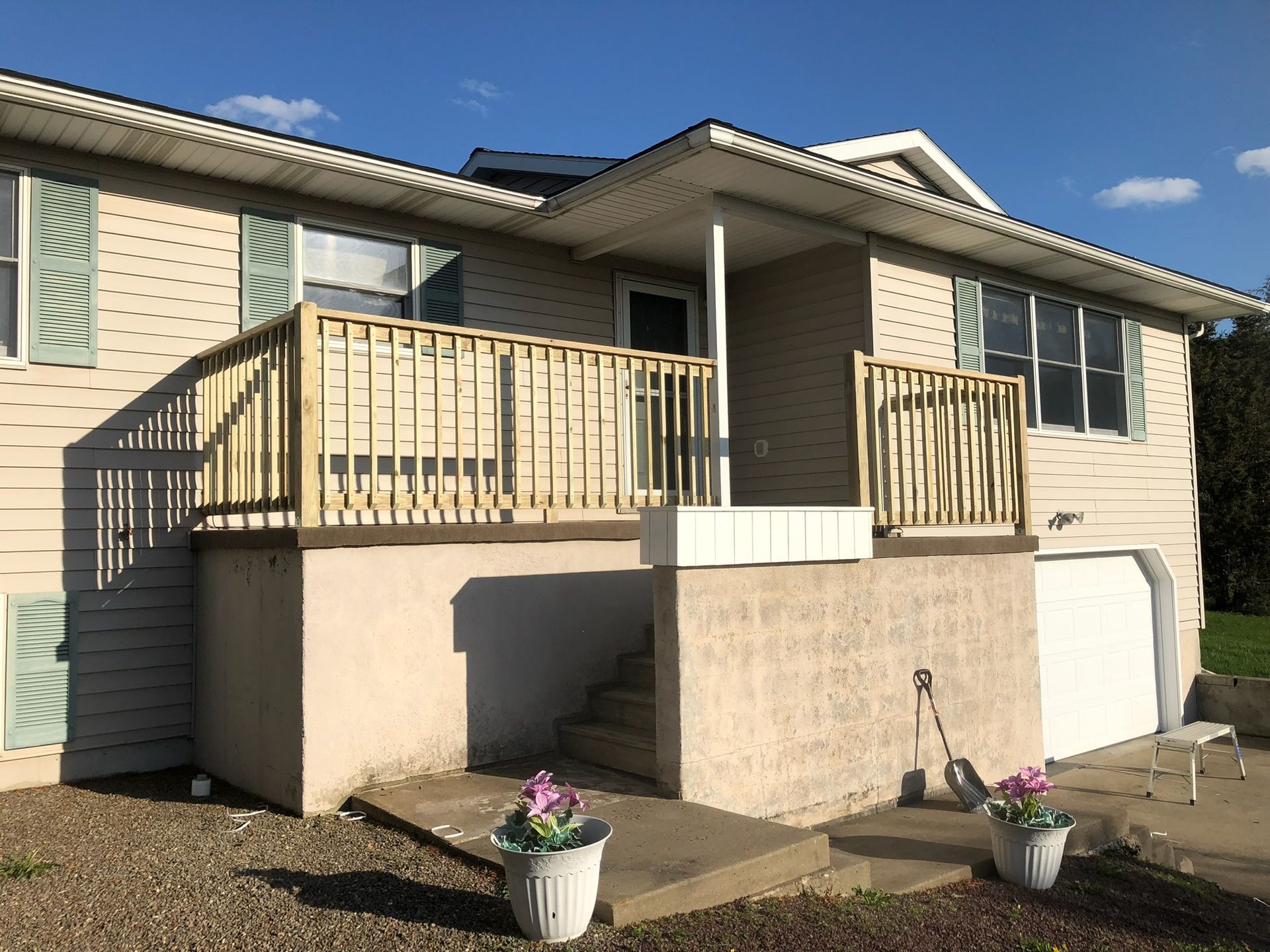 Front view of a beige house with a raised deck, white columns, and potted flowers by the entrance