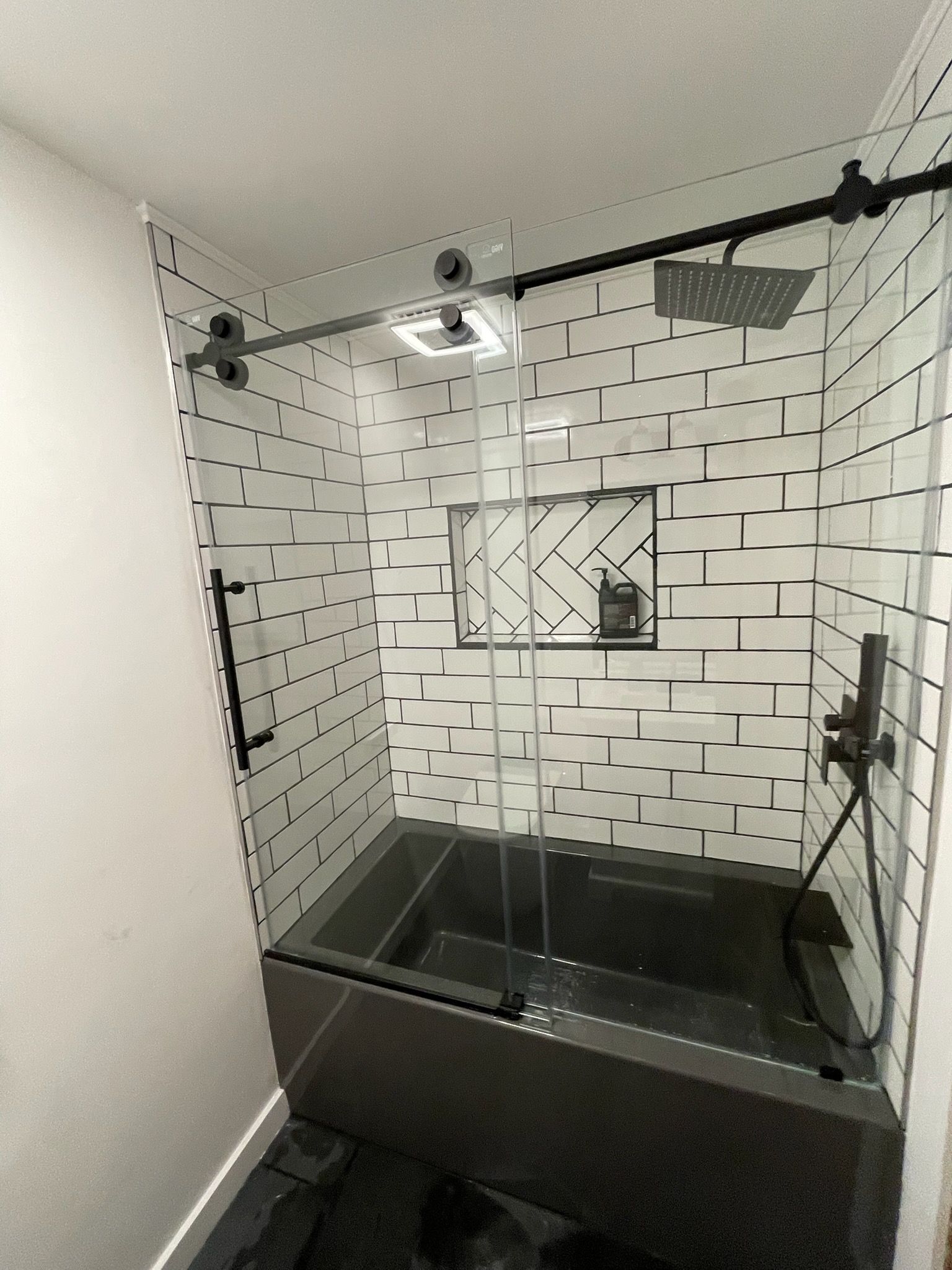 Modern black-and-white tiled shower with glass doors and a rain showerhead