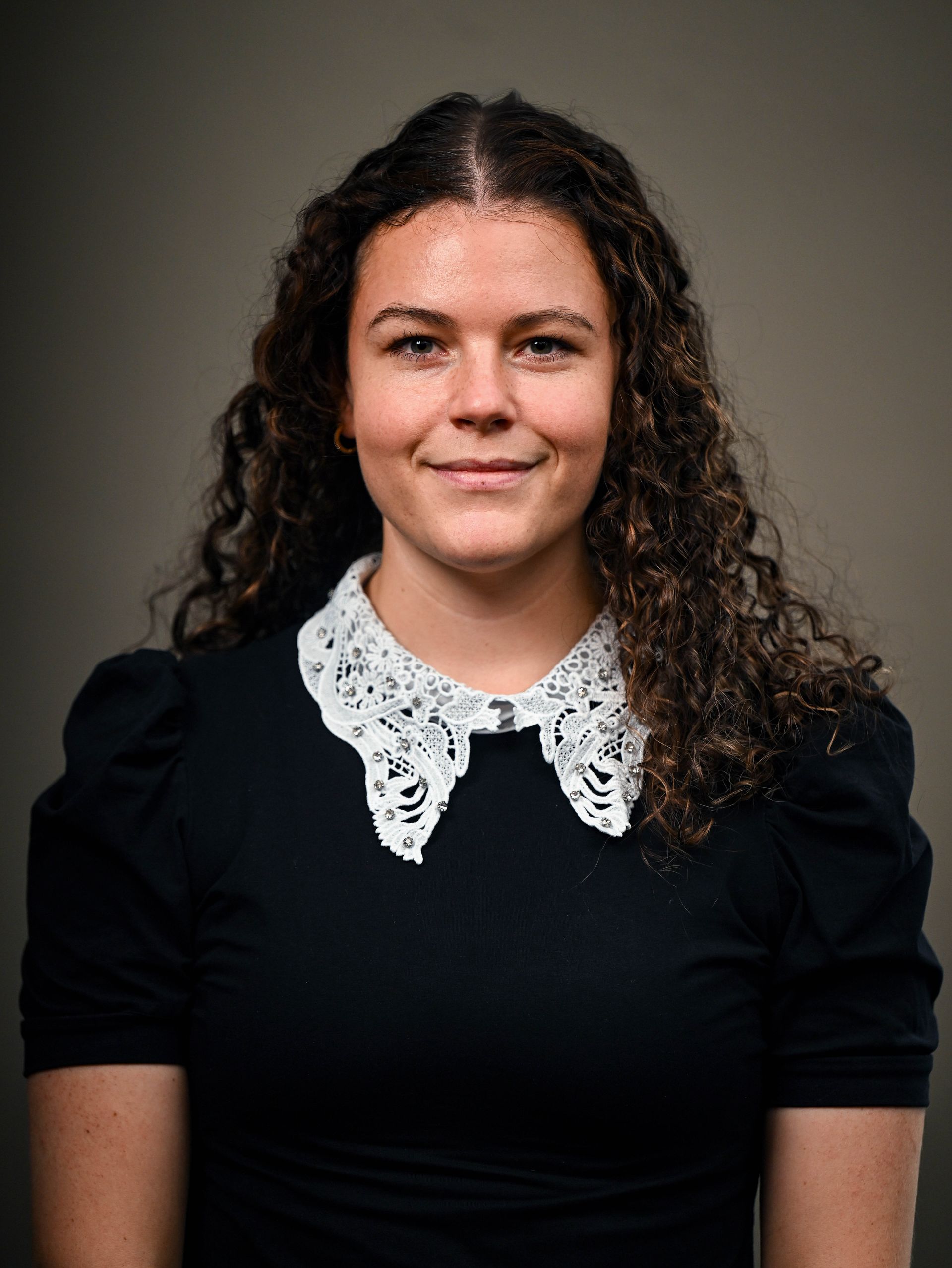 Woman with curly hair and white lace collar smiles at the camera.