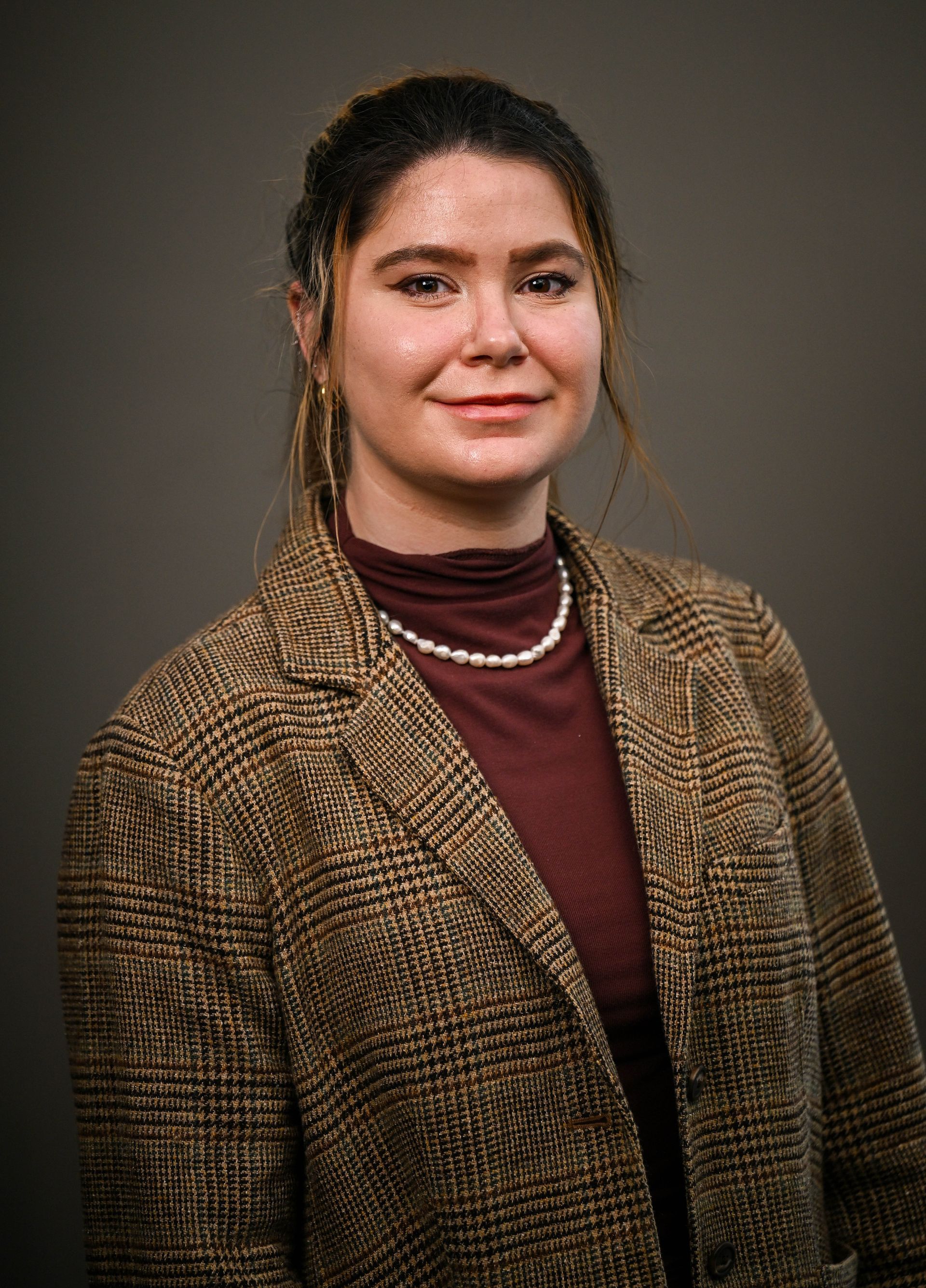Woman with brown hair wearing a plaid blazer, burgundy turtleneck, and pearl necklace, smiling at the camera.