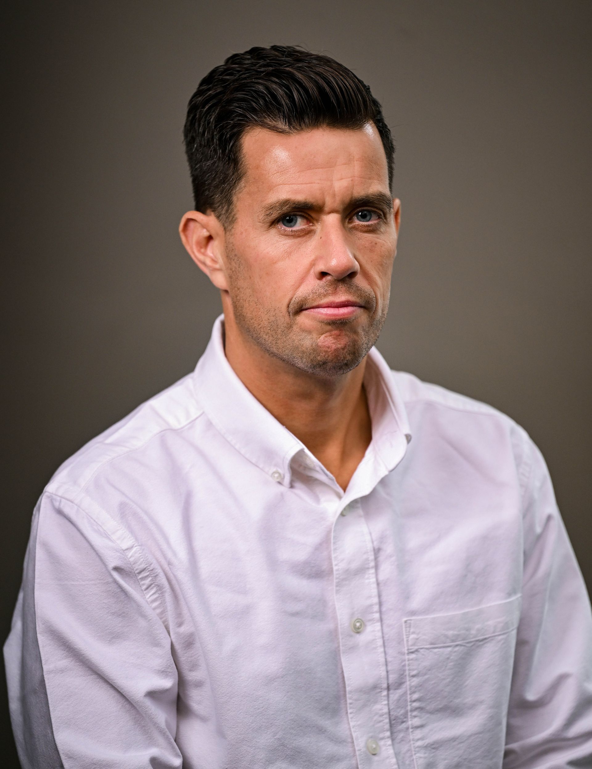 Man in white shirt, neutral expression, against a gray backdrop.