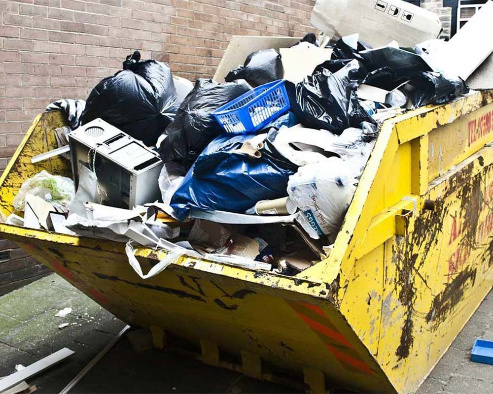 A yellow dumpster filled with garbage is sitting in front of a brick wall.