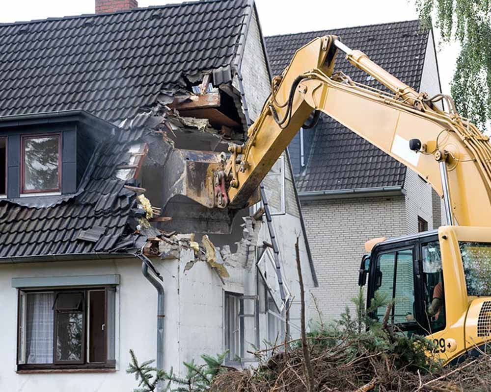 A yellow excavator is demolishing a house.