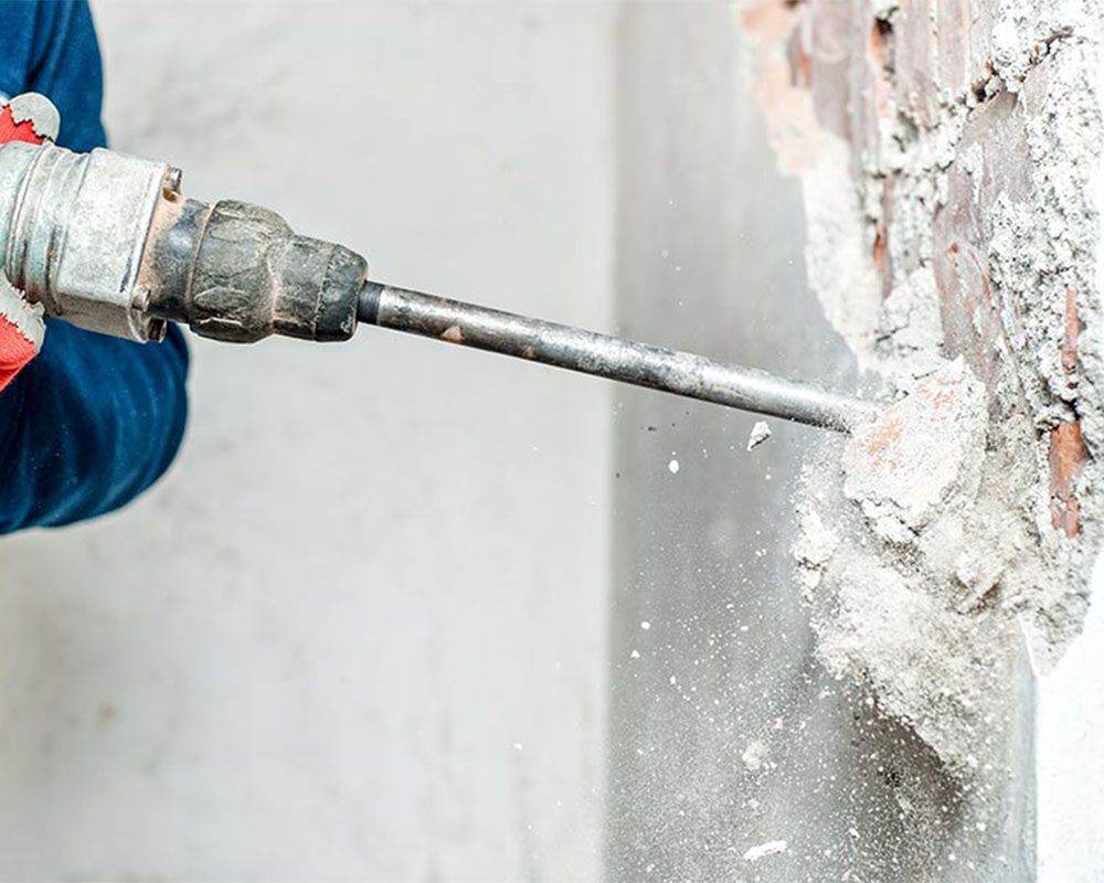 A man is using a hammer to drill a hole in a wall.