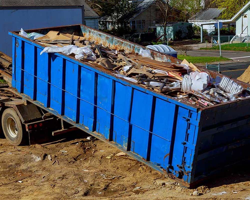 A blue dumpster is sitting on the ground next to a truck.