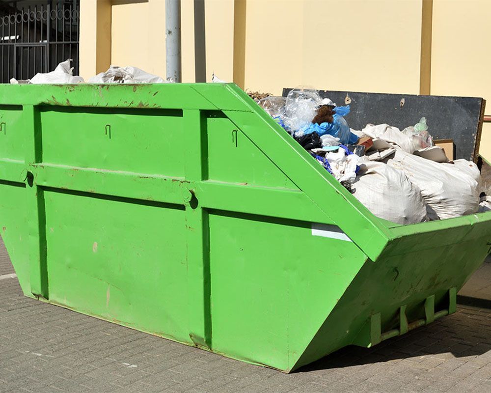A green dumpster filled with trash is parked in front of a building.