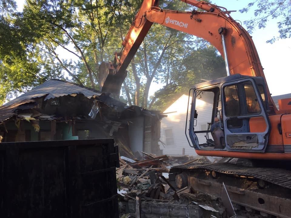 A large orange excavator is demolishing a house.