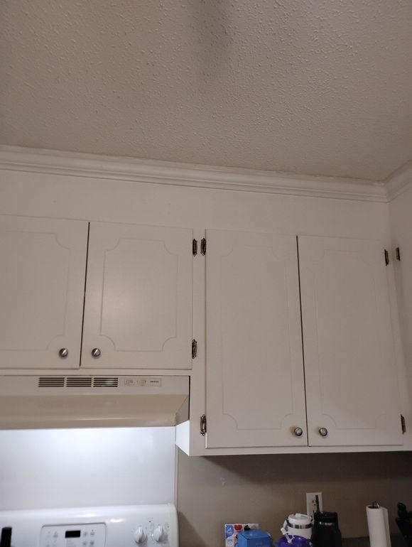 A low-angle view of white kitchen cabinets mounted on a wall with a popcorn ceiling above them.