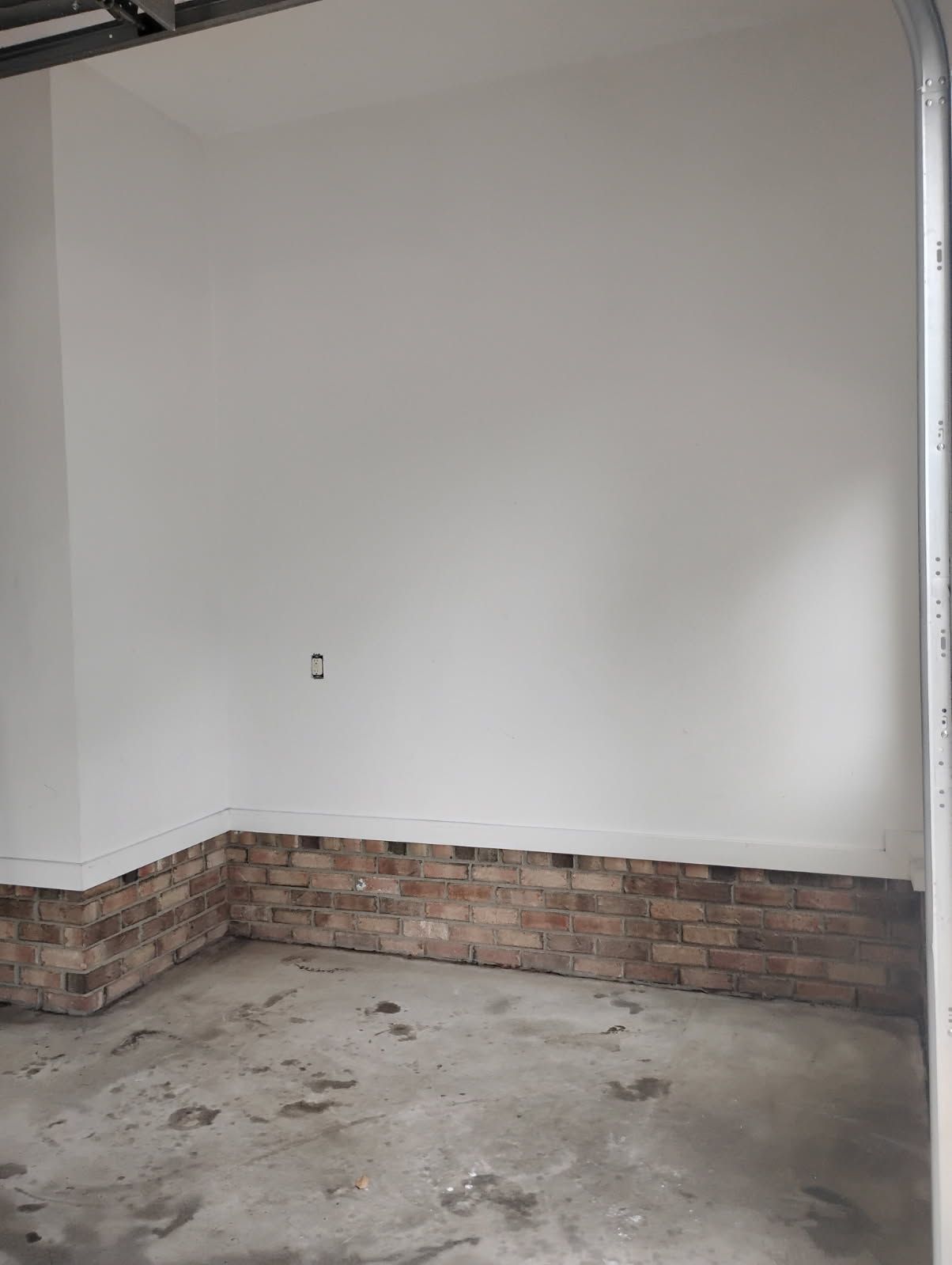 Empty indoor room with white walls, brick half-wall trim, and a concrete floor