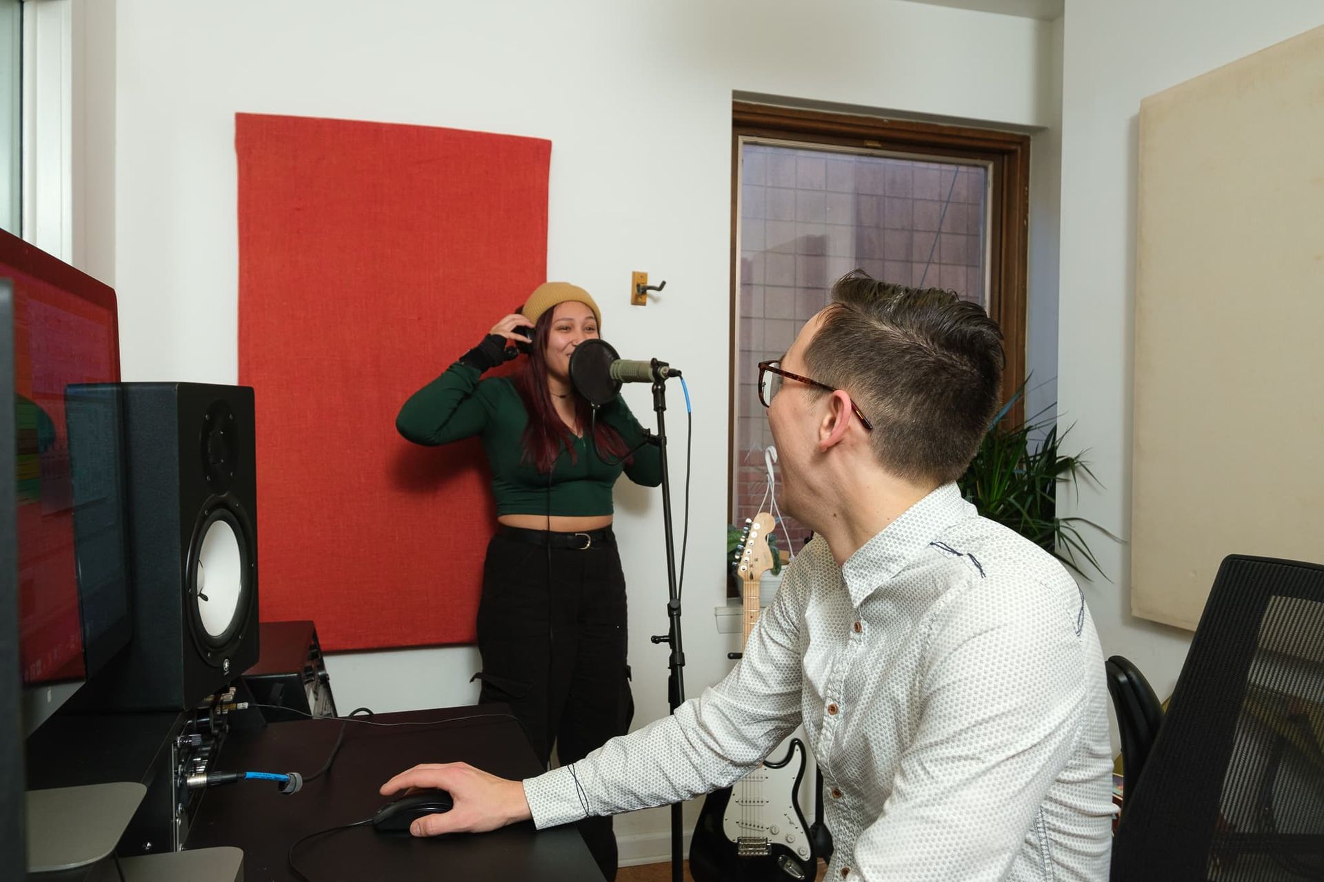 A man is sitting at a desk while a woman sings into a microphone.