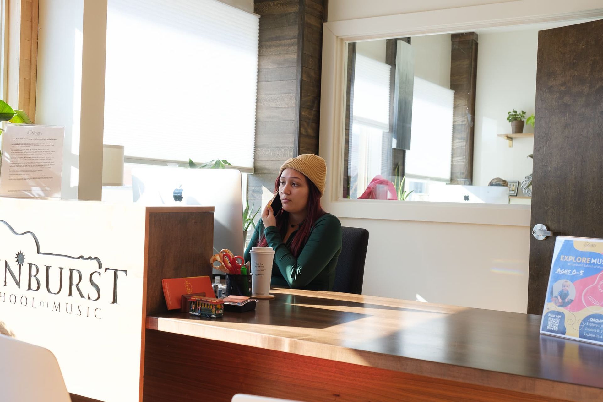 A woman is sitting at a desk talking on a cell phone.