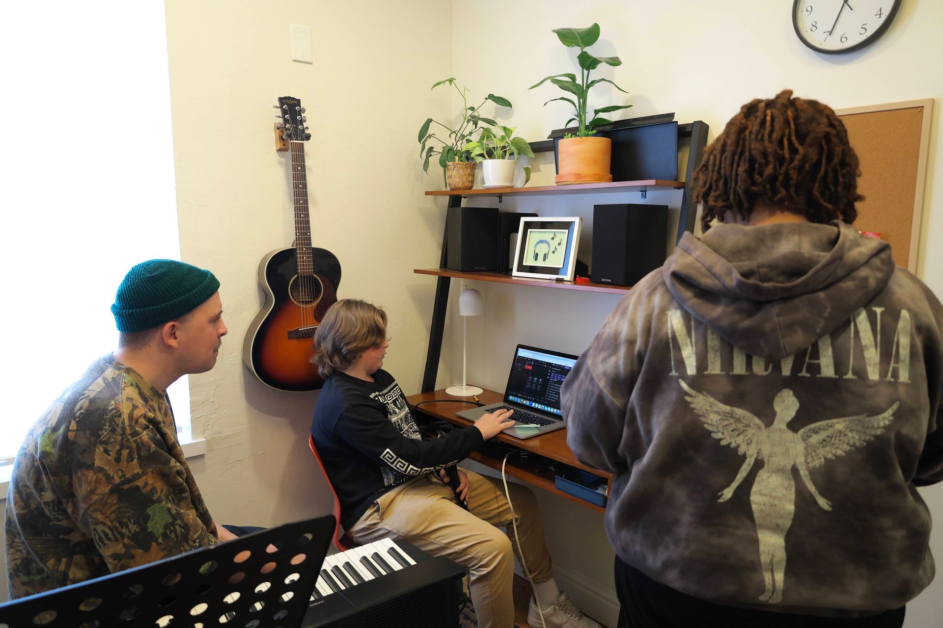 A man wearing a nirvana hoodie is standing next to two other people in a room.