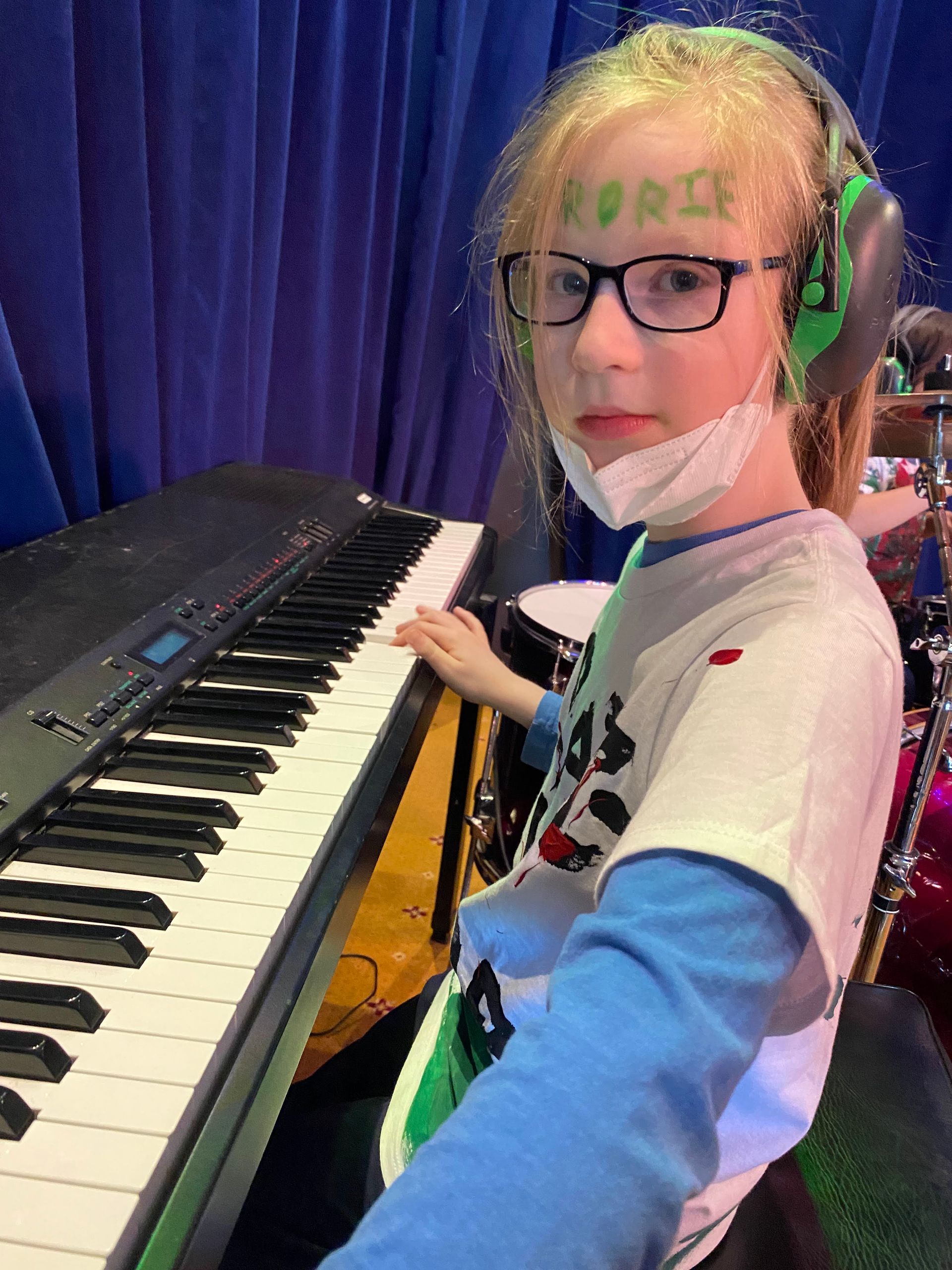 A young girl wearing a mask and headphones is playing a keyboard.