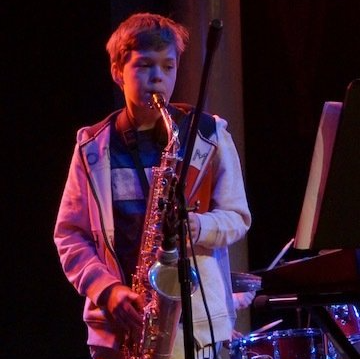 A young boy is playing a saxophone and singing into a microphone