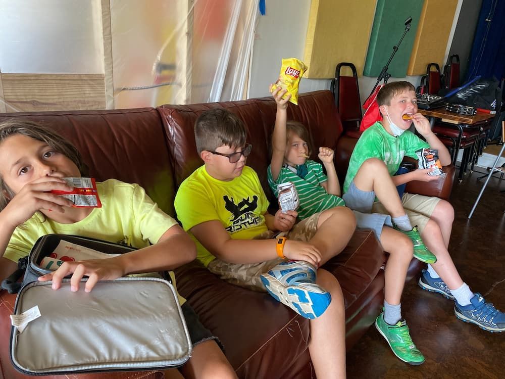 A group of children are sitting on a couch eating and drinking.