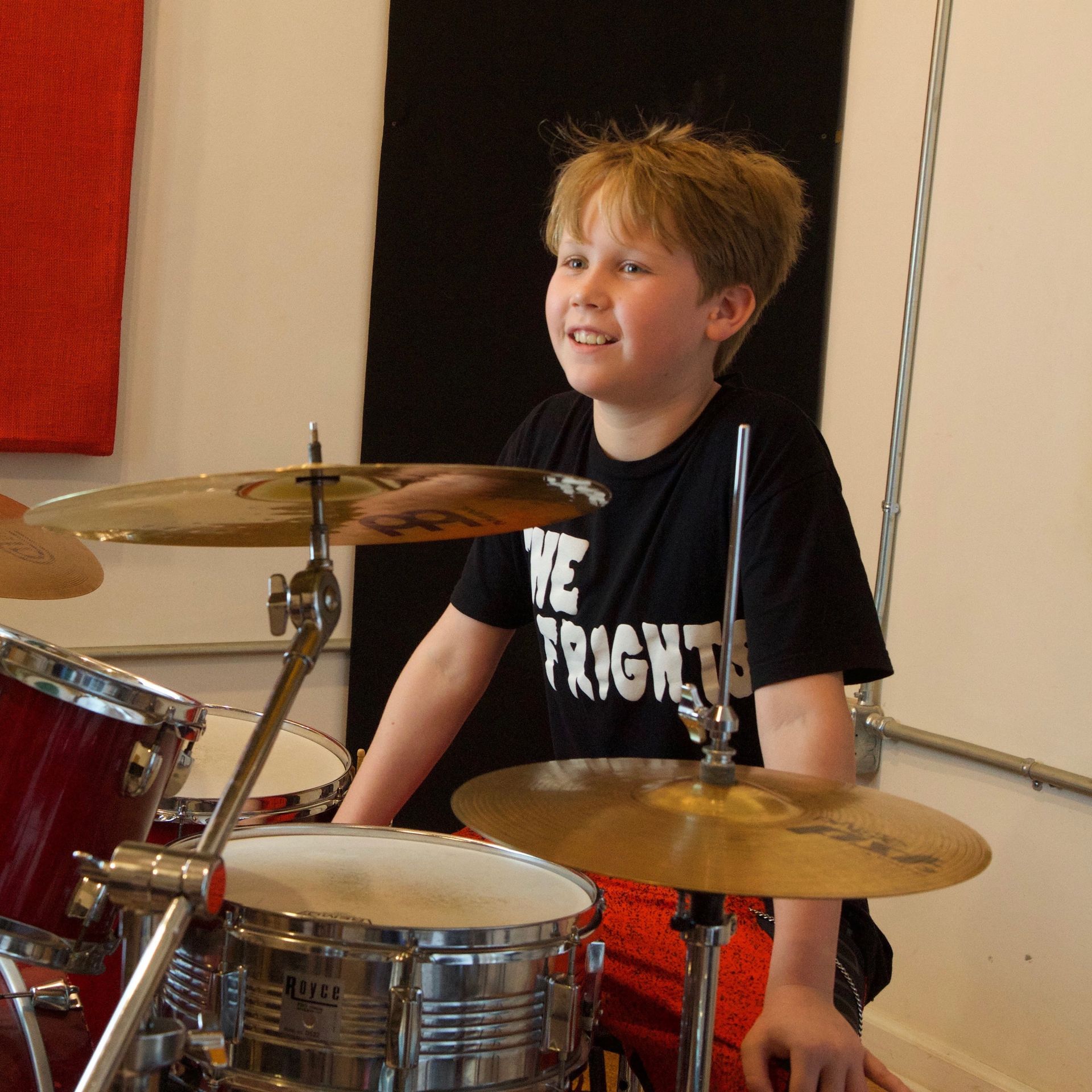 A young boy playing drums with a shirt that says we frighten