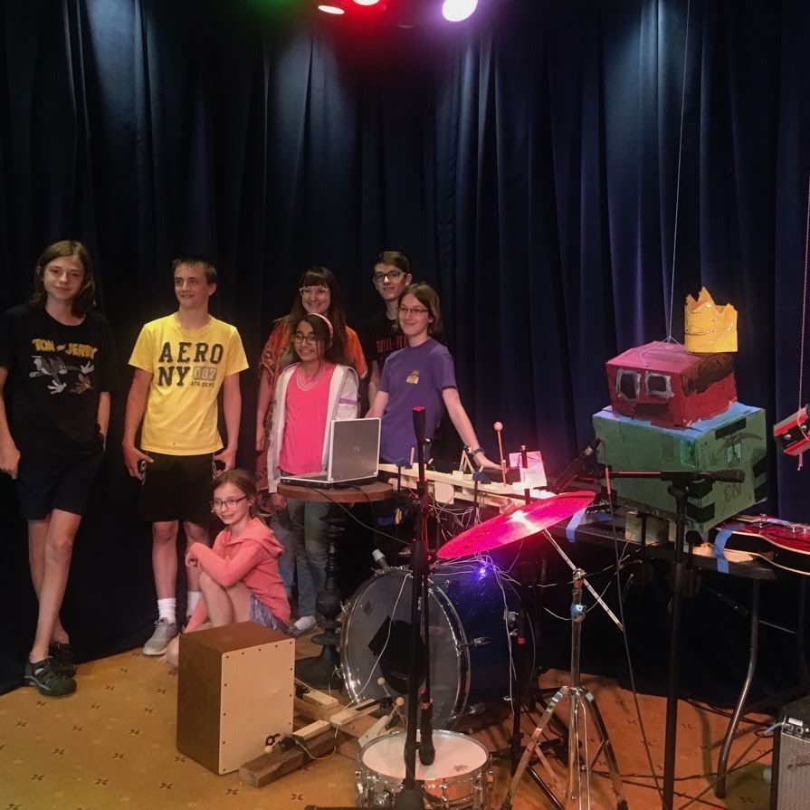 A group of people standing in front of a drum set with one wearing a yellow aero ny shirt
