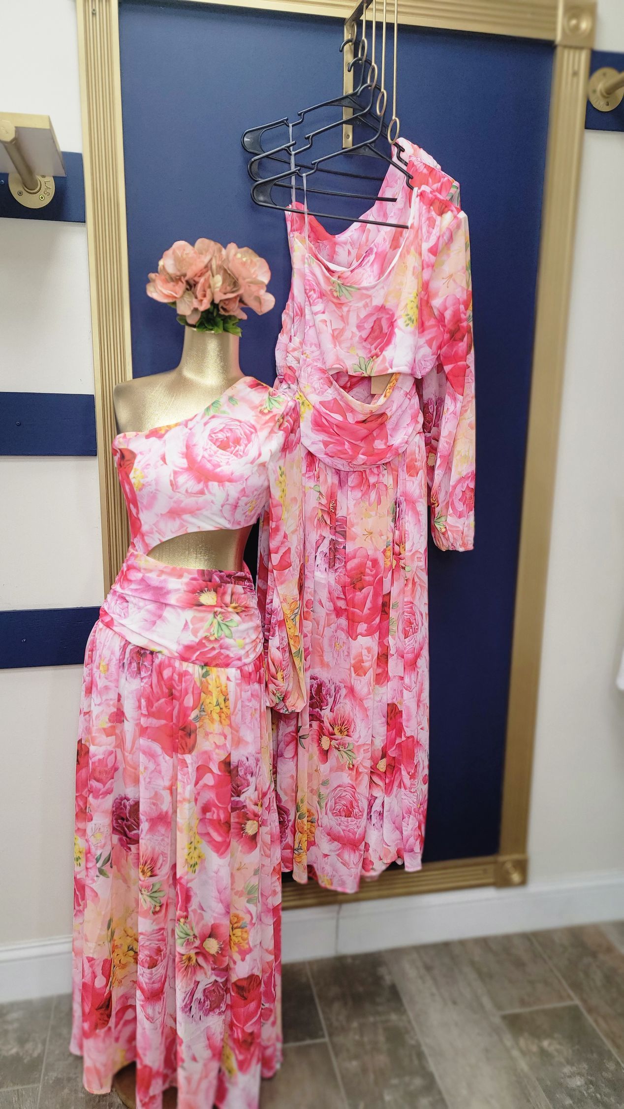 Pink floral outfit on a mannequin and a matching set hanging; against a gold-trimmed blue wall.