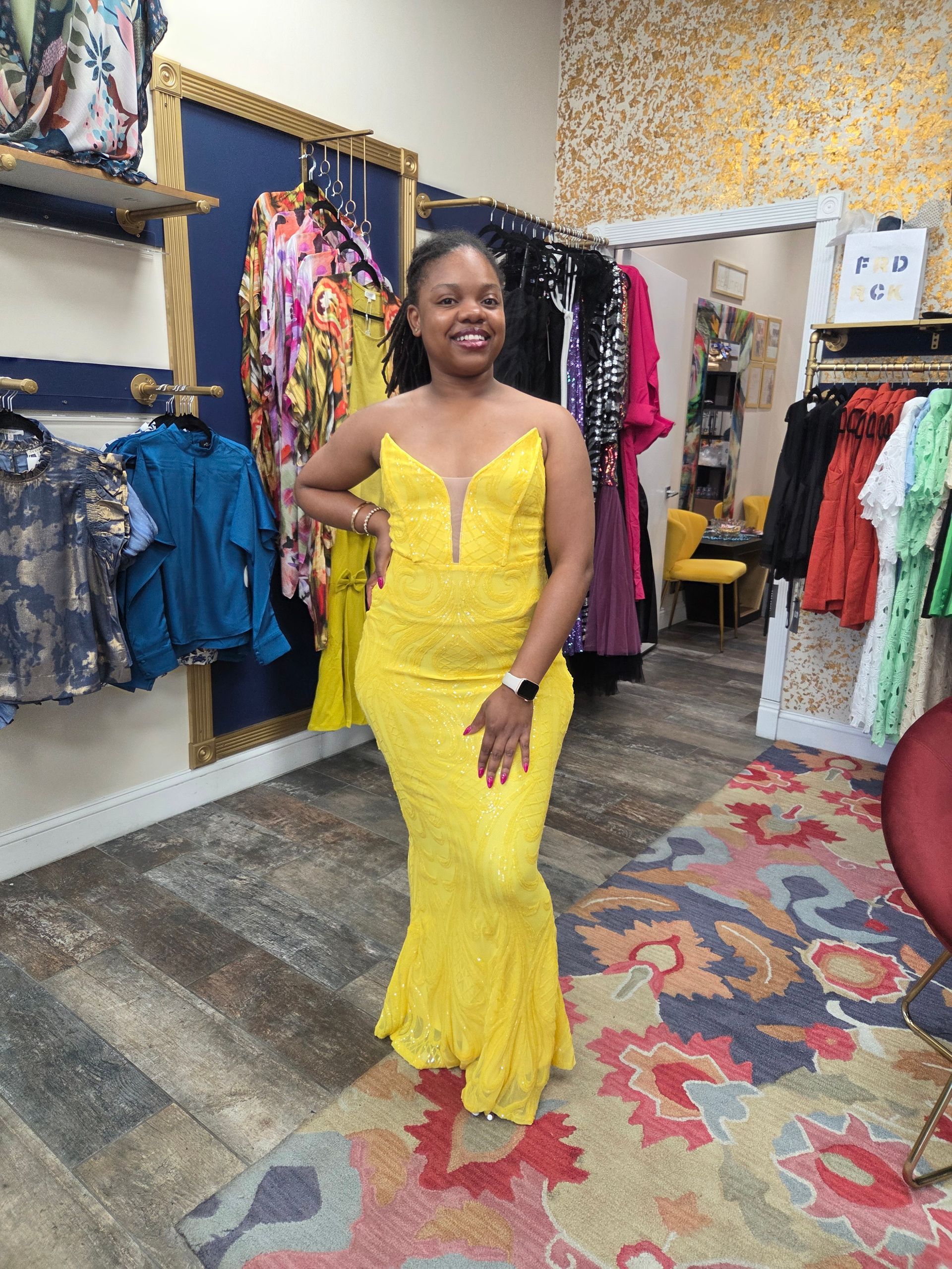 Woman in yellow sequined gown poses in a clothing store.