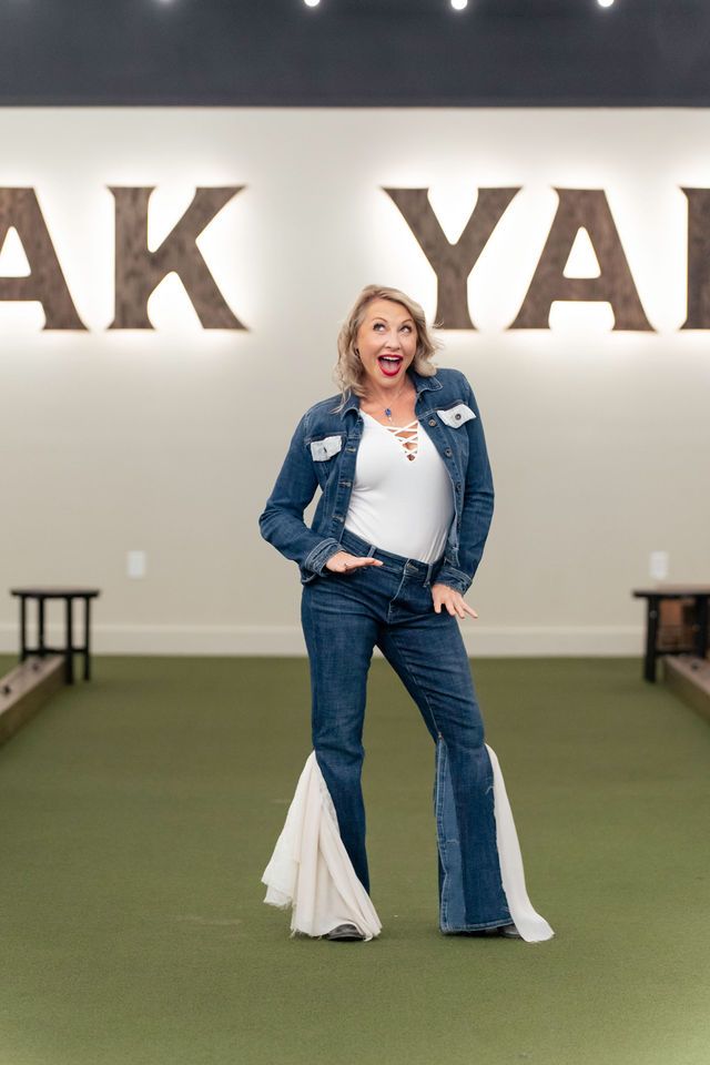 Woman in denim jacket and pants with white flares, posing in front of 