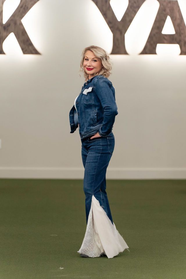 Woman in denim jacket and flared jeans with white lace panel, posing indoors.