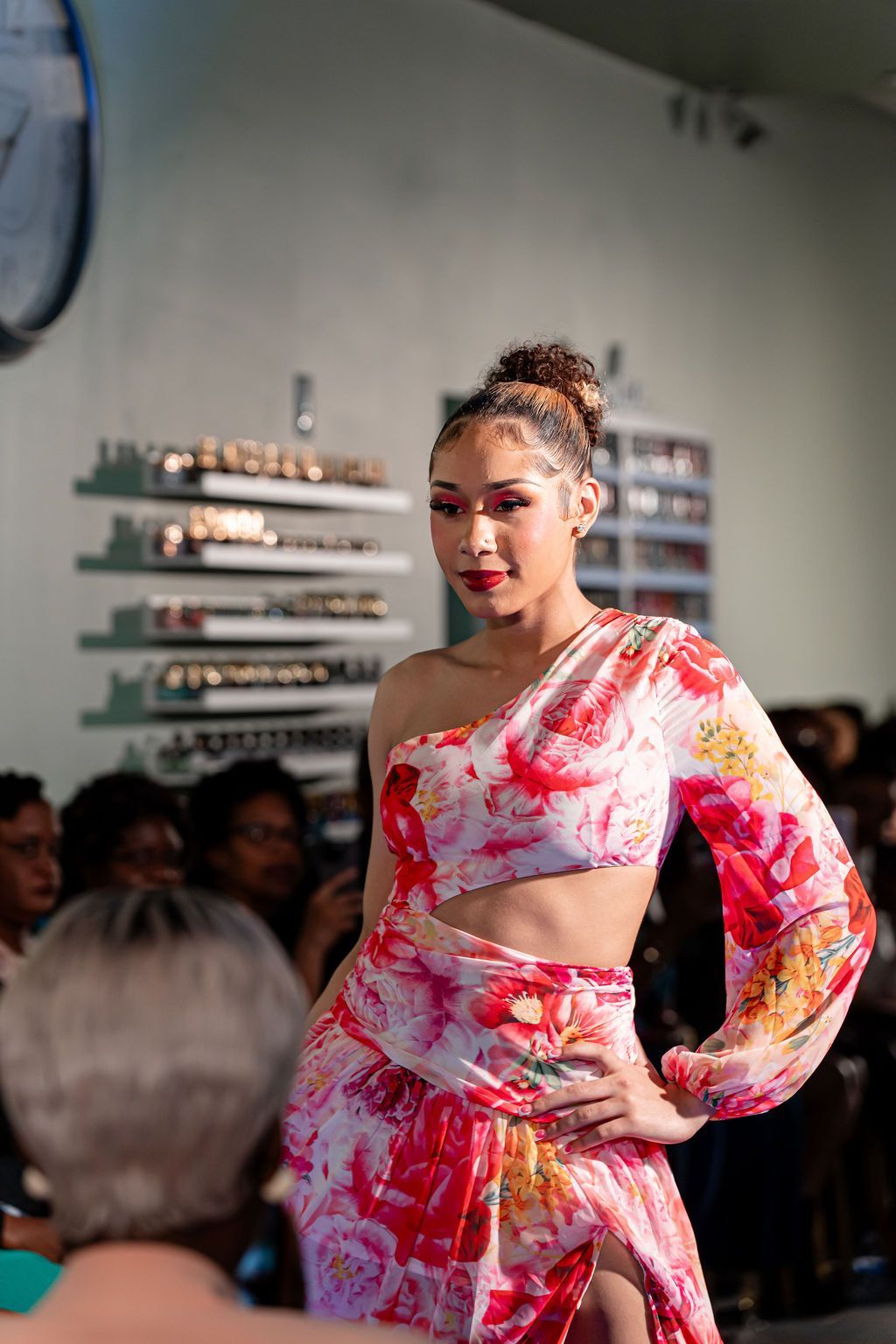 Woman with red and black braids smiles, wearing an olive green off-shoulder dress, sitting at a table in a restaurant.
