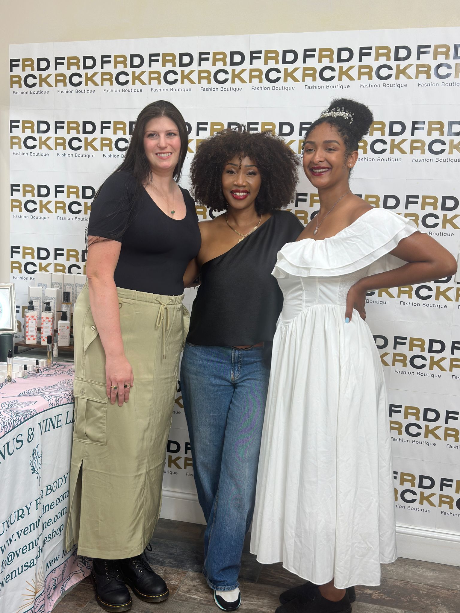 Three women pose in front of a backdrop for Frederick Fashion Boutique