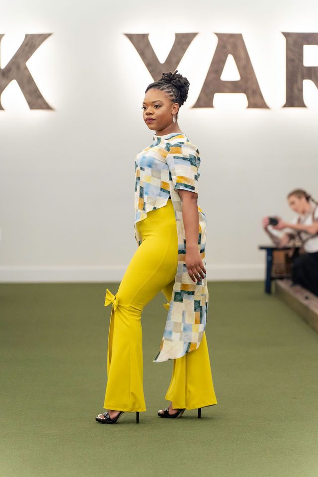 Woman in yellow pants and patterned top on a runway, looking to the side.