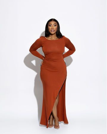 Woman in a long, rust-colored dress with a side slit stands against a white backdrop.