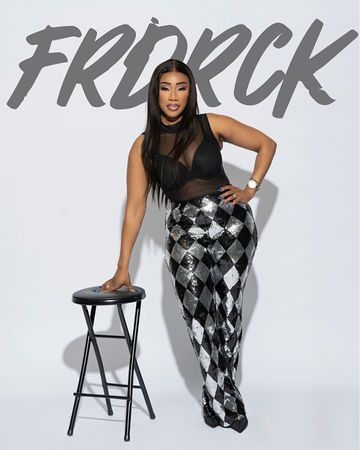 Woman in black top and sequined pants, leaning on a stool against a white backdrop. 