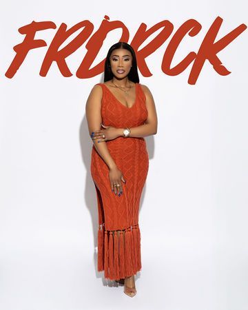 Woman in rust-colored dress with fringed hem stands against white background,