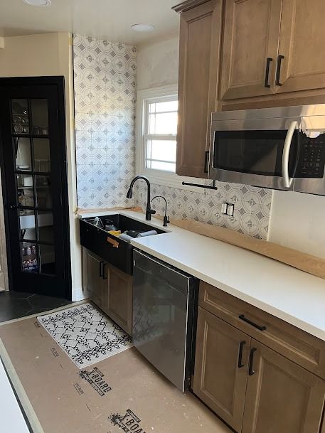 Kitchen with beige cabinets, white countertops, black sink and faucet, and a stainless steel dishwasher and microwave.