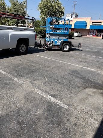A blue lift is hitched to a white truck in a parking lot on a sunny day.