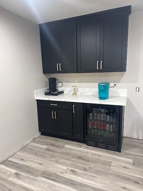 Black cabinets and mini-fridge in a small kitchen nook. White countertop, K-cup machine, and water cooler.