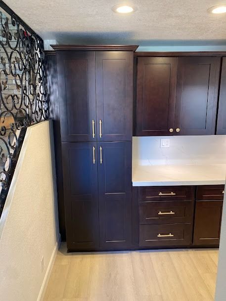Dark brown kitchen cabinets with gold hardware, next to a wall with a decorative railing and light wood flooring.