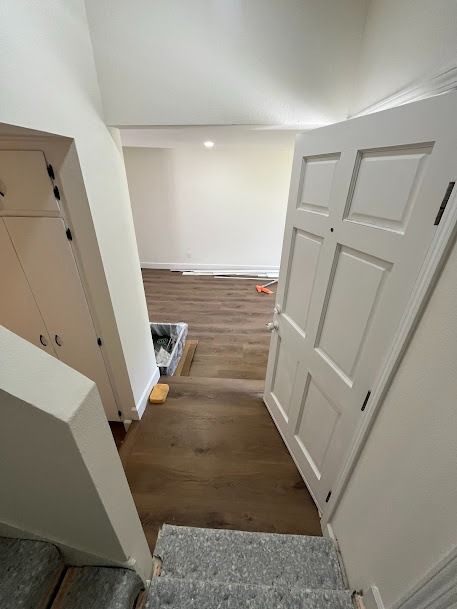 Staircase leading down to a room with a partially open white door, and wood flooring.