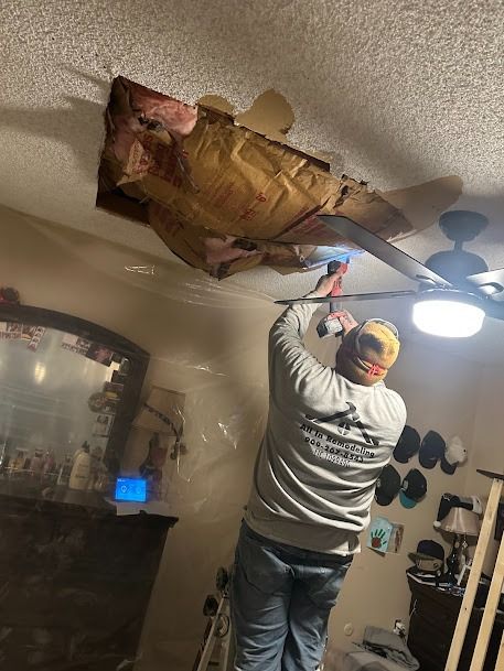 Man repairing ceiling. Ceiling damage shows insulation. Bedroom setting, ladder.