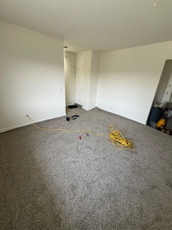 Empty room with gray carpet and white walls. Extension cord on the floor.