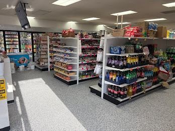 Interior of a convenience store with shelves stocked with products, bright lights, and a gray speckled floor.