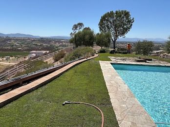 Lush green lawn beside a swimming pool, overlooking a valley, with a person in the distance.