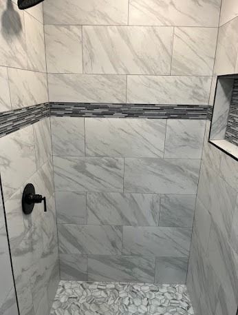 Shower with white and gray marble-look tiles, black fixtures, and a decorative horizontal band.