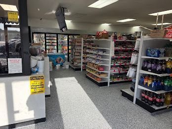 Interior of a convenience store with shelves of products, a cooler, and a checkout counter.