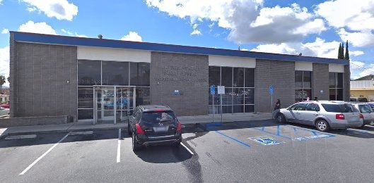A one-story building with large windows and a blue and white roof. Cars are parked in front of the building.