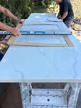 Two people using a level on a countertop. They are outside.