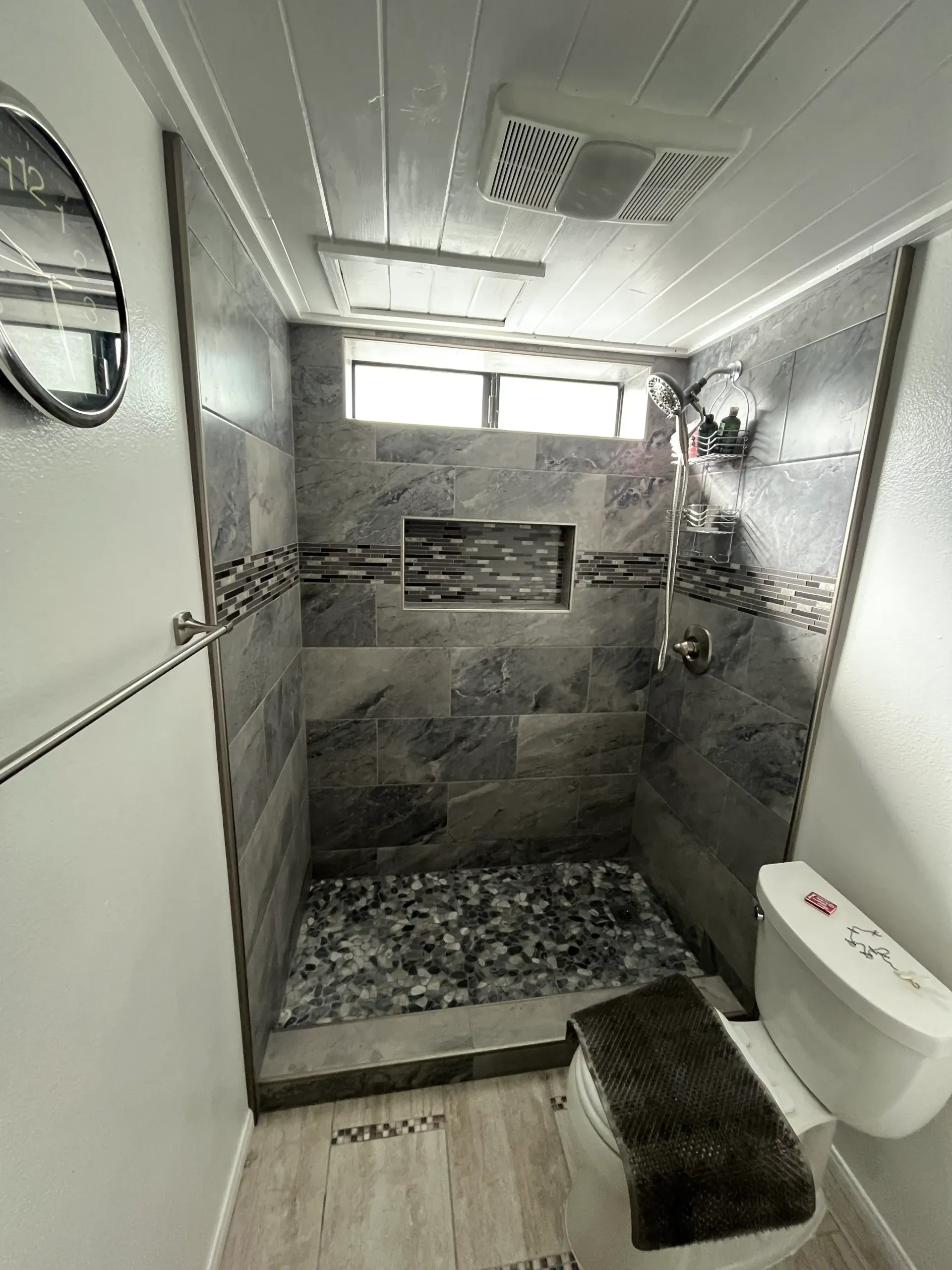 Small bathroom with stone shower, pebble floor, toilet, and towel rack.