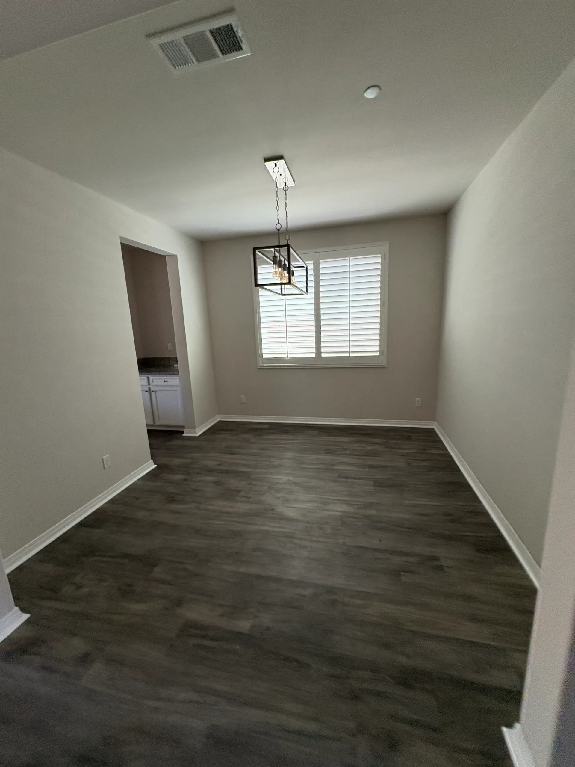 Empty dining room with dark wood floors, a window with shutters, and a light fixture.