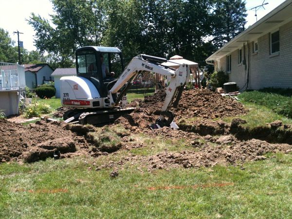 A bobcat excavator is digging a hole in a yard