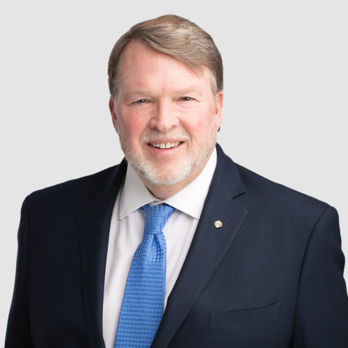 Man in a blue suit smiles at the camera against a gray background.