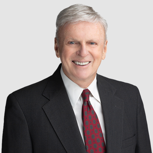 Man in a black suit smiles, wearing a red patterned tie.