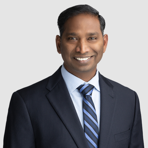 Man in suit smiling, with striped tie against light background.